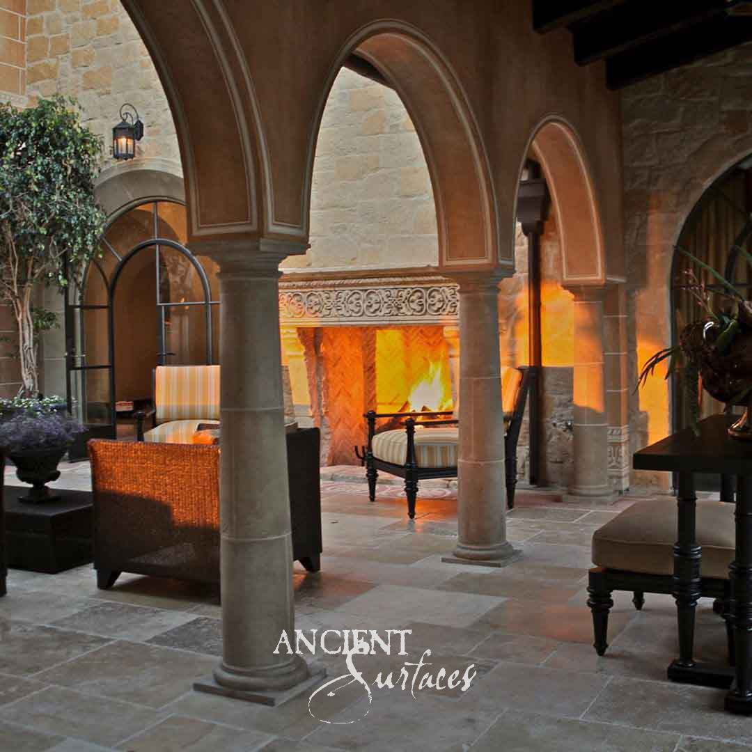 Wide reclaimed limestone fireplace mantel with a carved quatrefoil tracery frieze on its lintel, carried on shaped stone corbels above a herringbone firebox