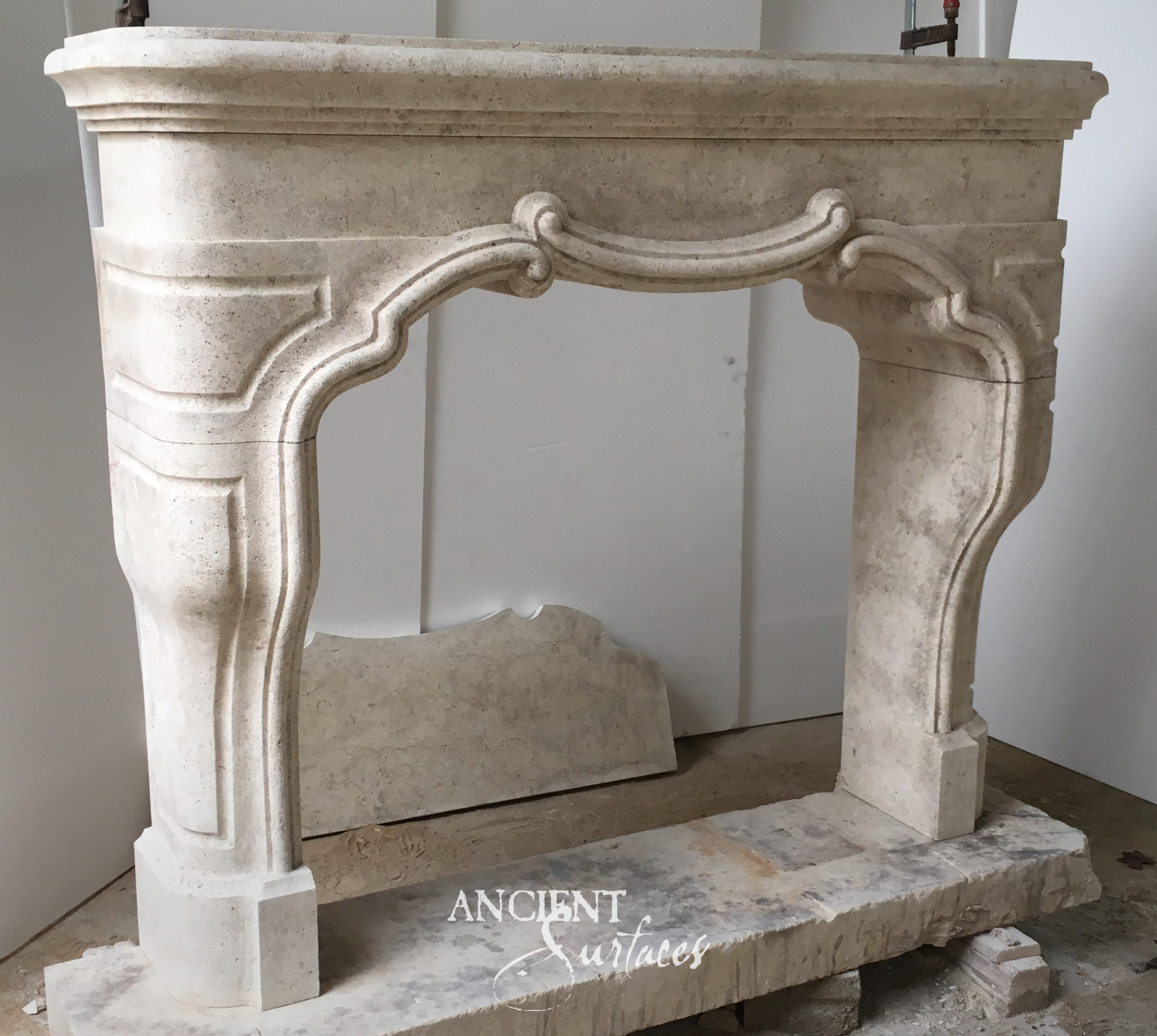 Ivory reclaimed limestone fireplace mantel with a serpentine arched opening, raised scrolled keystone and curved cabriole legs on square block feet
