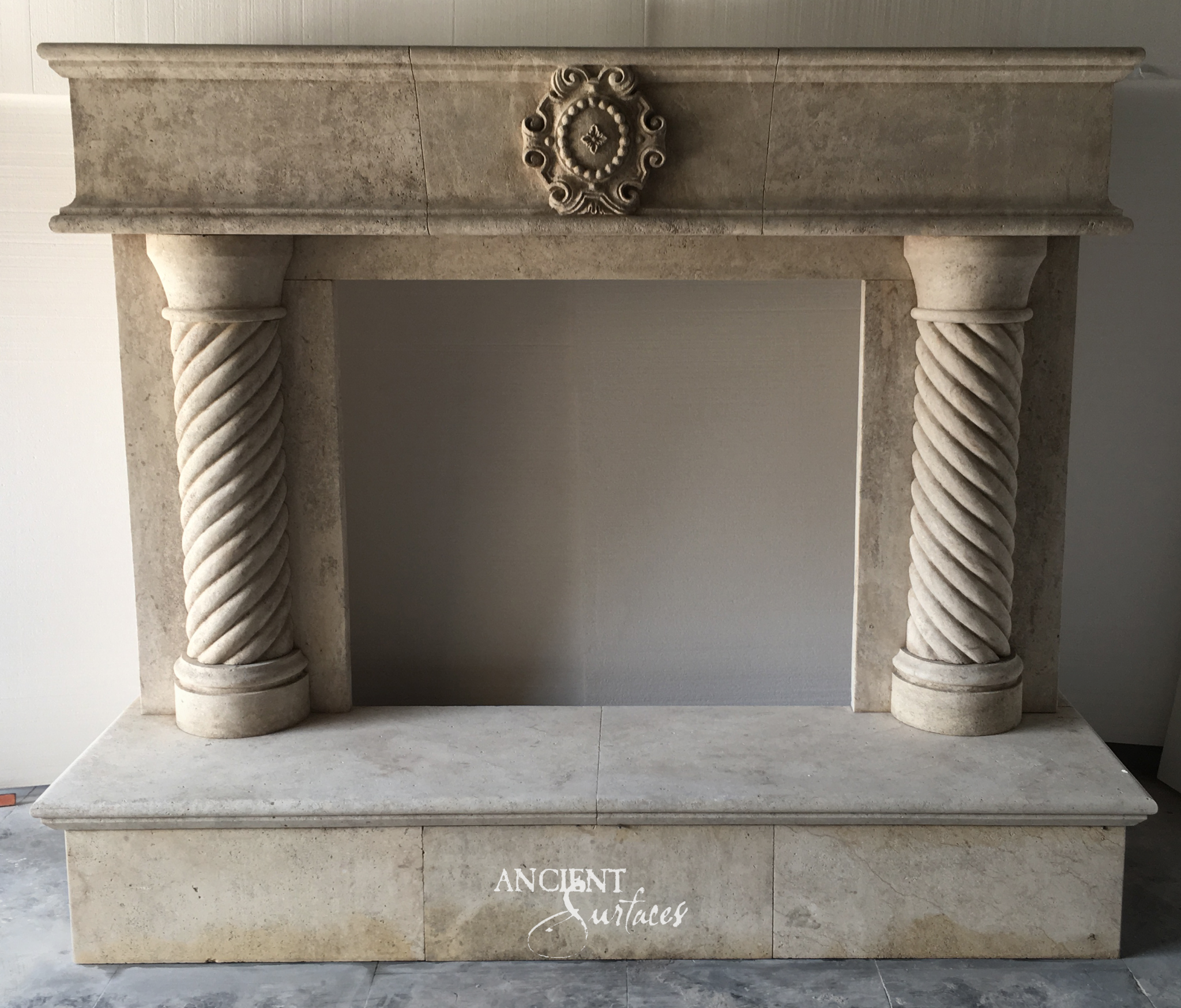 Reclaimed limestone fireplace mantel with a carved oval cartouche on a plain frieze and a pair of freestanding spiral twisted limestone columns as jambs